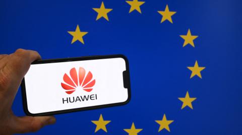 This illustration photograph taken in Brussels on March 13, 2025 shows Chinese telecom giant Huawei logo displayed on a smartphone in front of an European Union flag. Belgian police raided several addresses in the country as part of a probe into alleged corruption "under the guise of commercial lobbying", prosecutors said. "Several individuals have been arrested for questioning in connection with their alleged involvement in active corruption," the federal prosecutor's office said, adding that searches were also carried out in Portugal. Belgian newspaper Le Soir said the probe was linked to Chinese tech giant Huawei and its activities in Brussels since 2021. (Photo by Nicolas TUCAT / AFP)